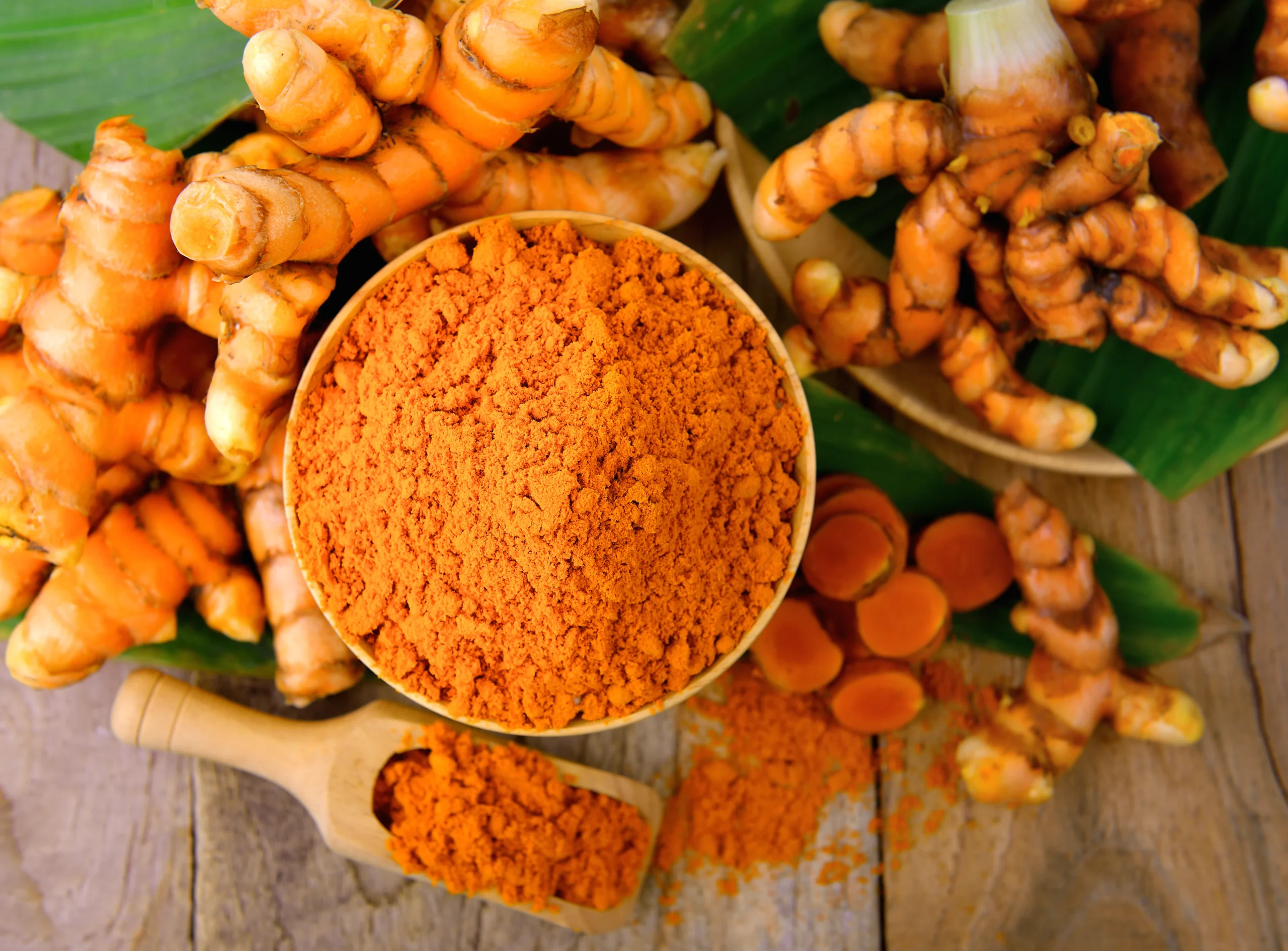 Turmeric powder, dried turmeric roots and supplement capsules arranged on a dark surface.
