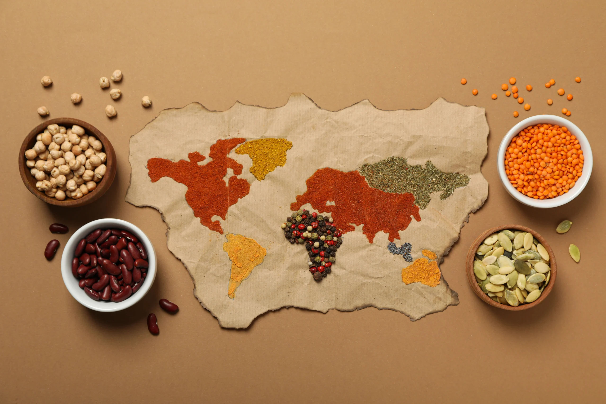 World map creatively made with colourful spices, pulses and legumes, surrounded by bowls of chickpeas, kidney beans, lentils and seeds.